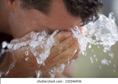 A man bends over and rejuvenates himself with a splash of cool, fresh water on his face.