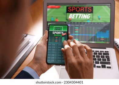 Man betting sports using smartphone   laptop at table  closeup  Bookmaker websites displays