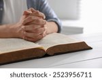 Man with Bible praying at white wooden table, closeup