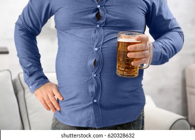 Man With Big Belly Holding Glass Of Beer At Home