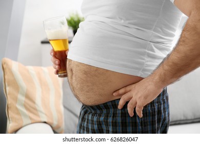 Man With Big Belly Holding Glass Of Beer At Home