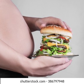 Man with a big fat belly cuddle and holding a plate with a high cheeseburger