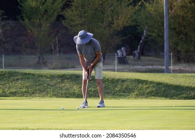 Man With A Big Sun Hat On His Head Playing Golf.