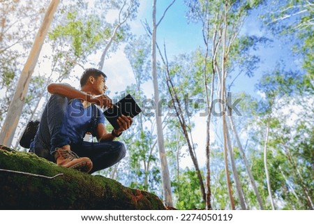 A man Biologist or botanist recording information about tropical plants in forest. The concept of hiking to study and research botanical gardens by searching for information. low angle view