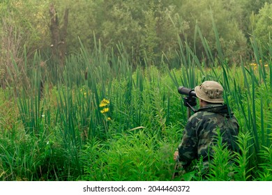 man birdwatcher makes field observation with a spotting scope standing among the tall grass