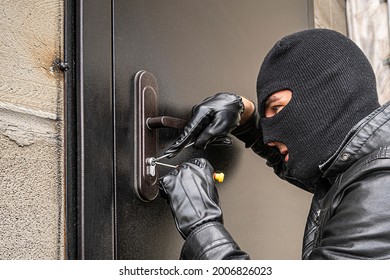A man in a black balaclava mask opens a locked door with a lock pick. The robber breaks into the house. Robbery of a private house. Criminal concept
