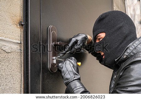 A man in a black balaclava mask opens a locked door with a lock pick. The robber breaks into the house. Robbery of a private house. Criminal concept