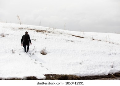 Man In A Black Coat Walking Up The Snowy Hill