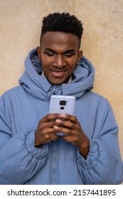 A man of black ethnicity with a phone and a blue jacket on a yellow background, looking at social networks or digital press
