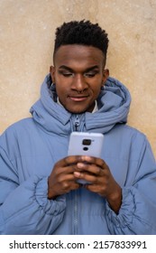A man of black ethnicity with a phone and a blue jacket on a yellow background, looking at social networks or digital press