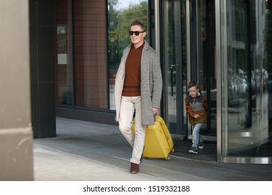 Man in black glasses, with a yellow suitcase in beige trousers, in a gray coat, leaves the hotel. - Shutterstock ID 1519332188