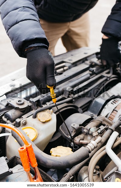 Man in black gloves\
checking the oil level in a car outdoors in winter. Car mechanic\
engineer working in car repair service. Male hands fixing a car,\
checking the oil level.