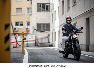 Man With Black Hair Riding His Black Motorbike To Go To Work In The City, With A Red Helmet Between Buildings