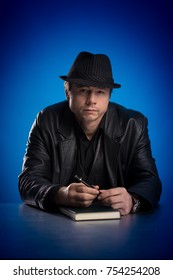 Man in black hat posing at table on blue background
