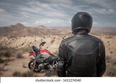 A Man In Black Helmet And Black Leather Jacket Standing Near Adventure Motorcycle In Desert, Adventure Overland Travel, Back View