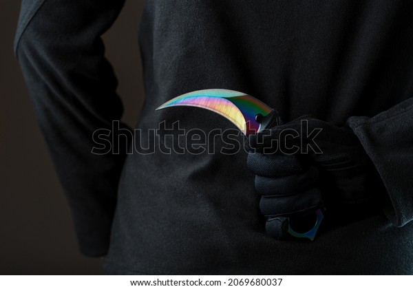 The man in\
black holds a curved kerambit knife behind his back. A criminal\
with a knife hidden behind his\
back