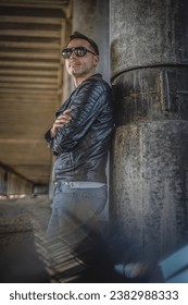 Man in the black leather jacket posing outdoors.