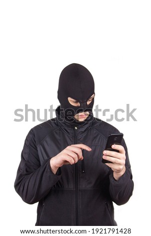 a man in a black mask with a cell phone and a laptop is engaged in Internet fraud