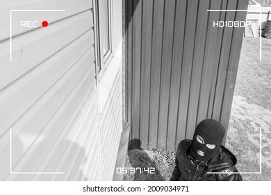 A man in a black mask is trying to rob a house.  The robber noticed a security camera. Robbery of a private house. Criminal concept. Simulation of recording from a surveillance video camera.