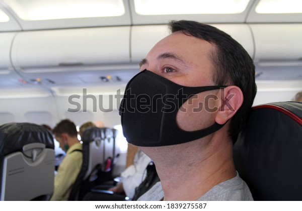 A man in a black\
protective mask in the cabin. The concept of protecting and\
preserving health during flights. The concept for safe travel\
during the pandemic covid-19