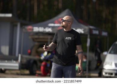 A Man In A Black Shirt And Blue Jeans Standing On A Skateboard, A Balding Man In Black Shirt Holding Cell Phone.