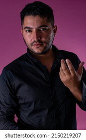 A man in a black shirt, posing on a pinkbackground looking at the camera with a surprised gesture. Emotions, joy and fun of men.
