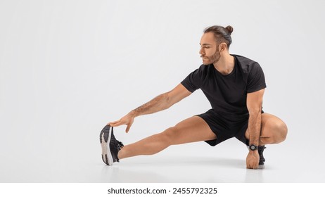 A man in a black shirt and shorts is engaged in a stretching exercise outdoors. He is stretching his arms, legs, and back to improve flexibility and prevent injury. - Powered by Shutterstock