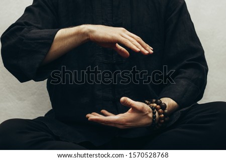  A man in black shirt sitting and doing qigong. Hands direct energy. Prayer, gratitude.Practicing monk. Qi energy. Yoga pose. Healing retreats. Close up.