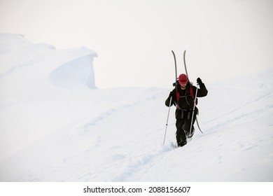 man in a black ski suit with trekking poles walks through deep powdery snow on a mountain slope