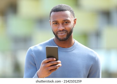 Man with black skin looks at you holding phone in the street