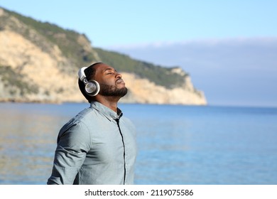 Man With Black Skin Meditating On The Beach With Headset On Summer