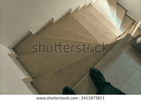 A man in black sneakers begins to descend the steps of the staircase, which spiral in the direction of movement in a clockwise direction. The Concept of Top-Down Descent.