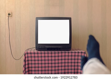 Man in black socks watches old TV with empty white screen for mockup. Entertainment concept.