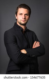 Man In Black Suit In Front Of A Grey Background Looking Serious