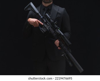 Man In Black Suit Holding Assault Rifle. Secret Service Man In Black Suit, Bodyguard Or Special Forces Agent Man With Gun Isolated On Black Background. Spy, Police Man In Black Suit No Face Visible.