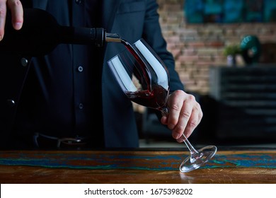 Man in black suit and black shirt pouring red wine into wine glass. Close up image of man holding wine glass, pouring red wine. - Powered by Shutterstock