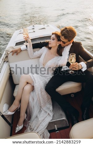 Man in a black suit and sunglasses hugs a woman on a yacht on a sunny day. Couple drinking champagne and having fun
