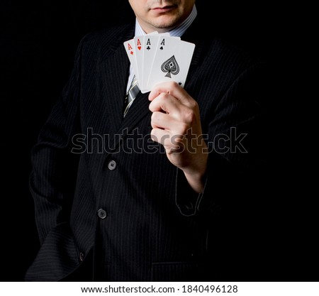 A man in a black suit and a tie holds 4 aces in his hand with black background. Poker cards. Play in poker and gambling games. Use for gambling sites, articles, advertising, gifts.