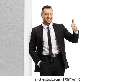 Man In A Black Suit And Tie Leaning On Wall And Showing Thumbs Up Isolated On White Background