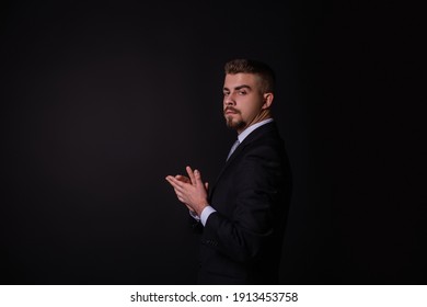 A Man In A Black Suit And A White Hill On A Black Background With A Sly Look. Businessman