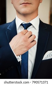a man in a black suit and white shirt straightens his tie with his hands, a close-up without a face