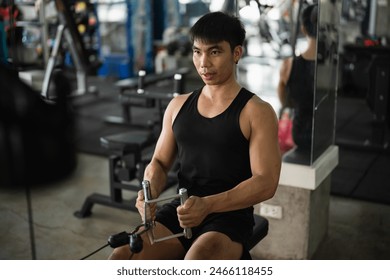 A man in a black tank top works out on a seated row machine in a modern gym. His serious expression and muscular build emphasize his dedication to fitness and strength training. - Powered by Shutterstock