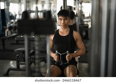 A man in a black tank top works out on a seated row machine in a modern gym. His serious expression and muscular build emphasize his dedication to fitness and strength training. - Powered by Shutterstock