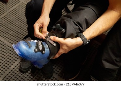 Man With Black Trousers Preparing To Ski Putting On His Blue Boots.