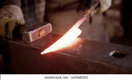 A man blacksmith forging a hot knife blade with a hammer - Powered by Shutterstock