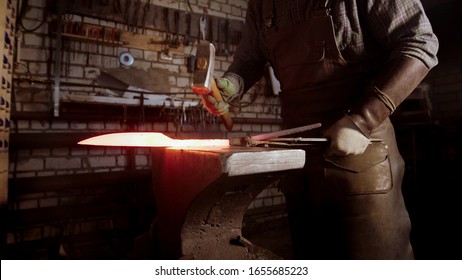 A man blacksmith forging a knife blade using a hammer