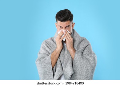 Man With Blanket Suffering From Runny Nose On Light Blue Background