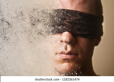 A man with a blindfold over his eyes disintegrates into dust.
