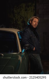 Man With Blond Hair In A Jeans Jacket Stands By An American Classic Muscle Car.