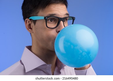 Man blowing up balloon on blue background. portrait of young man blowing blue balloon